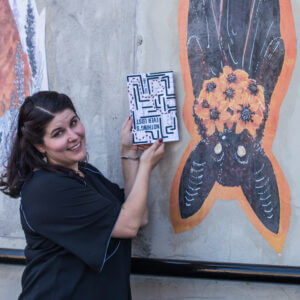 Emma G Rose holds up a book next to a mural of a bat