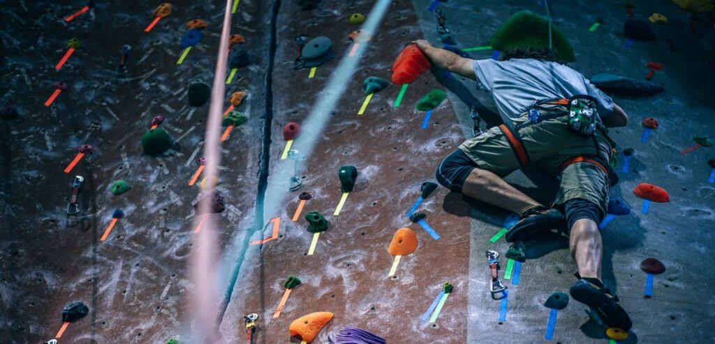 man climbing a rock wall with colorful handholds