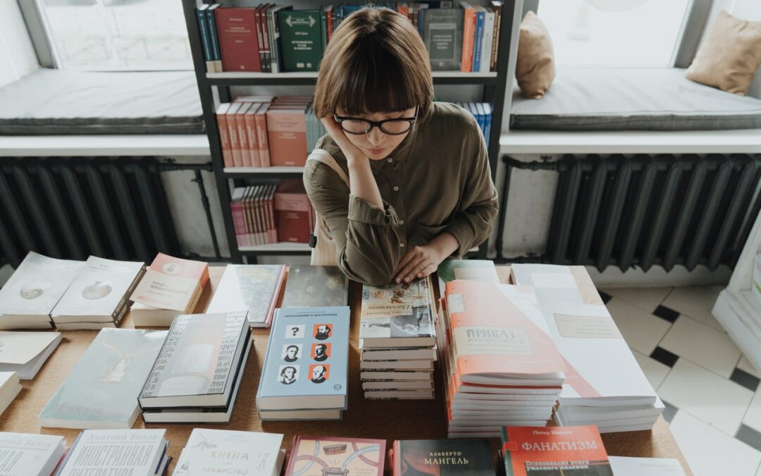 woman leans over a table stacked with books