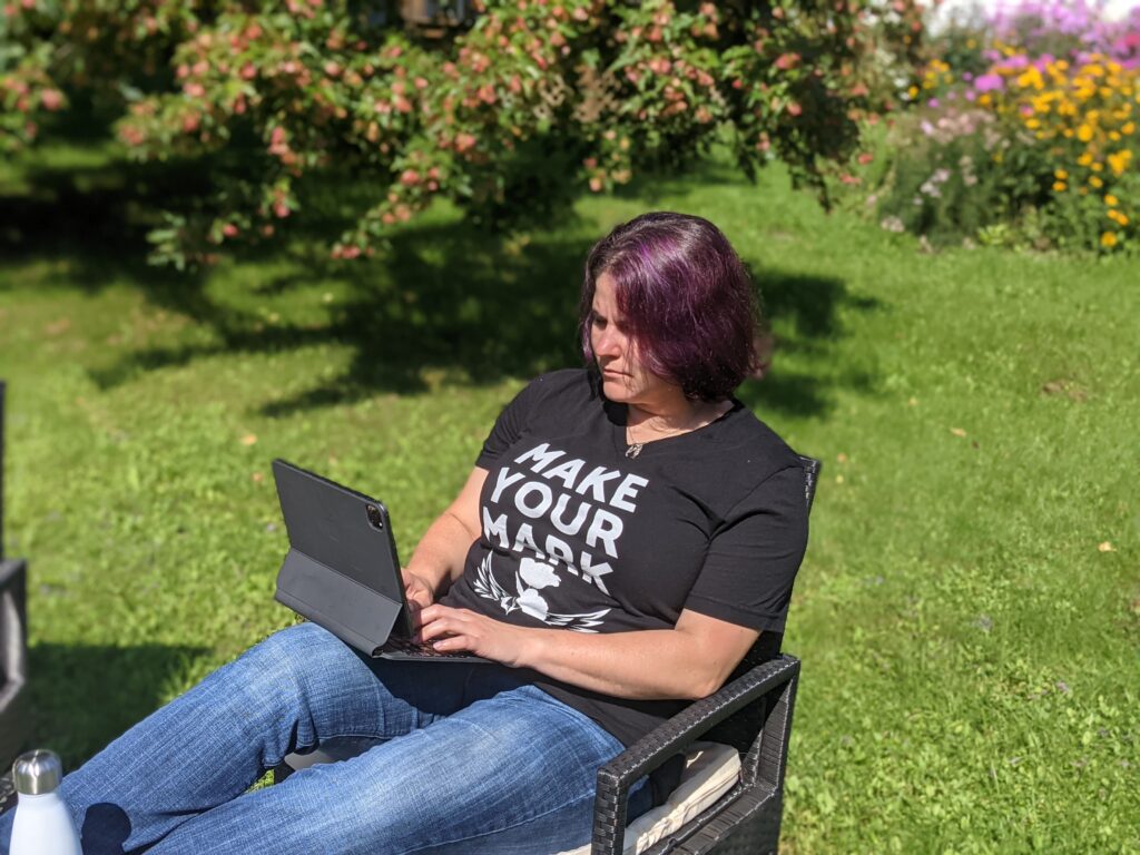 author Emma G Rose sits outdoors on a sunny day with a tablet on her lap